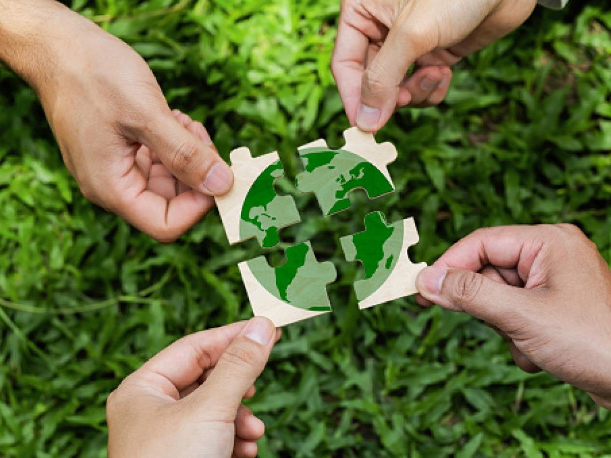 Hands holding 4 puzzle pieces depicting the earth