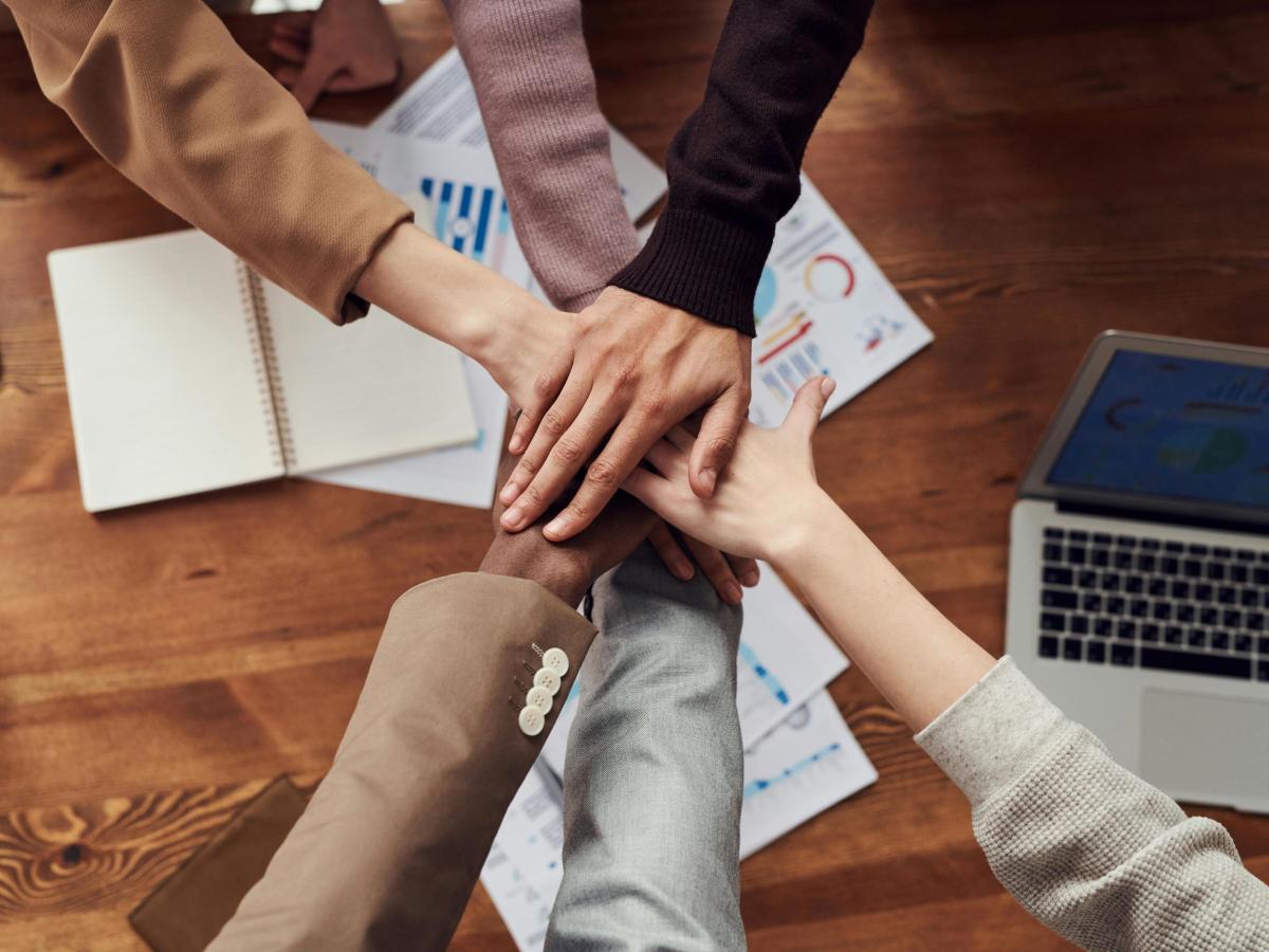 Team members stack hands above project meeting table