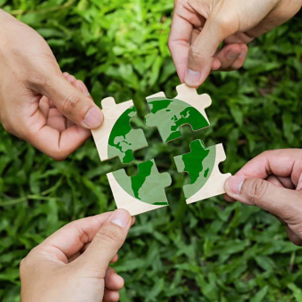 Hands holding 4 puzzle pieces depicting the earth